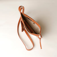 Brown leather clutch bag with a zipper on a light beige background