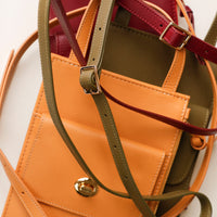 Close-up of a tan leather handbag with gold hardware on a light gray background