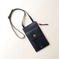 Black crossbody bag with a gold clasp on a light beige background