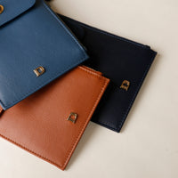 Three leather wallets in blue, brown, and black on a light beige background