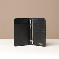 Front view of a open danilos travel pro passport case in black leather lux with 8 card slots a zipper compartment, a pen and 1 passport slot in brown pebble leather in a beige background