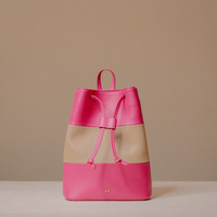 A colorblock leather backpack in vibrant pink and beige, featuring a drawstring closure and a small gold logo on the front, set against a neutral beige background.