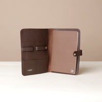 Front view of an open brown Danilos pebble leather inkspirator with a clip closure, a notebook inside, and organized pouches for pens on a beige background