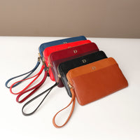 A collection of leather pouches with wrist straps in various colors aligned in a row.