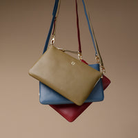 Stack of three leather handbags in green, blue, and red on a beige background