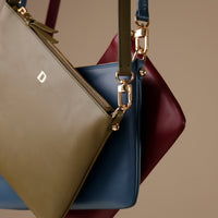 Close-up of a beige, blue, and burgundy handbag with gold zipper pulls on a neutral background.