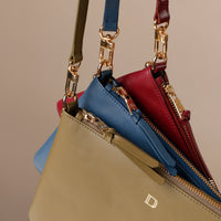 Three handbags in beige, blue, and red with gold zippers on a beige background.