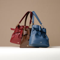 Three handbags in red, brown, and blue with bow details on a beige background