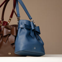 Blue handbag with a bow and brown handbag with a bow on a neutral background