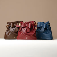 Three handbags in brown, red, and blue colors, featuring a ribbon design on the exterior and a magnetic closure.