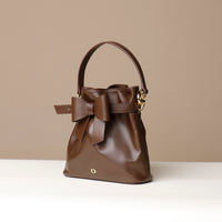 Brown leather handbag with a bow on a beige background