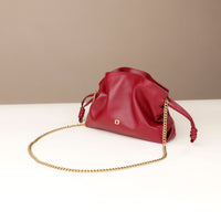 Red handbag with a gold chain on a white surface with a beige background