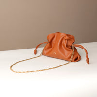 Brown leather drawstring bag with a gold chain on a white surface and beige background