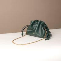 Green leather handbag with a gold chain on a white surface and beige background