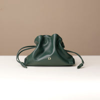 Green drawstring bag on a white surface with a beige background