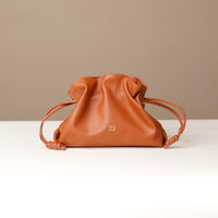 Brown leather drawstring bag on a white surface with a beige background