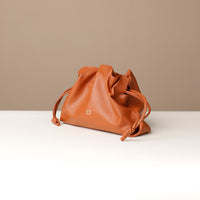 Brown leather drawstring bag on a white surface with a beige background