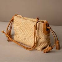 Sassy Satchel 26 Raffia Mostaza handcrafted with raffia and premium leather, with a mostaza leather strap, in a beige background, lateral view