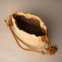 An open Sassy Satchel 26 Raffia Mostaza handcrafted with raffia and premium leather, with a mostaza leather strap, in a beige background, upper view

