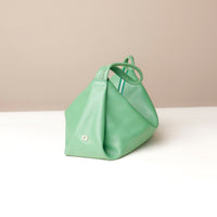 Green handbag on a white surface with a beige background