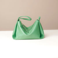 Green handbag on a white surface with a beige background