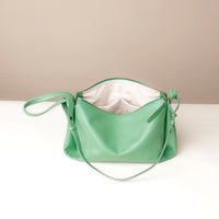 Green handbag on a white surface with a beige background