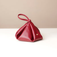 Red handbag with a gold clasp on a white surface with a beige background