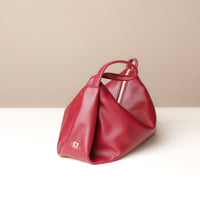Red handbag with a gold zipper on a white surface with a beige background