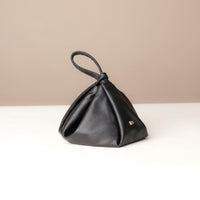 Black leather handbag on a white surface with a beige background