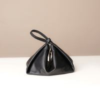 Black leather handbag on a white surface with a beige background