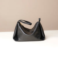 Black handbag on a white surface with a beige background