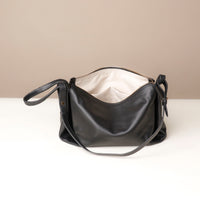 Black leather handbag with a beige interior on a white surface.