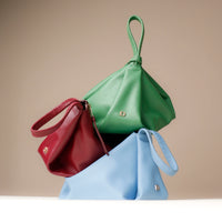 Three handbags in green, red, and blue on a beige background