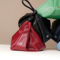 Red, black, green, and blue leather bags with visible brand initials on a neutral background