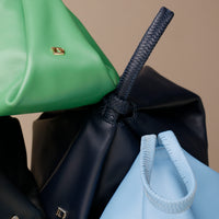 Close-up of green, black, and blue bags with handles on a beige background