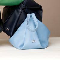 Light blue handbag with a black bag in the background on a neutral surface