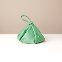 Green handbag on a white surface with a beige background