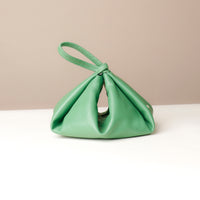 Green handbag on a white surface with a beige background