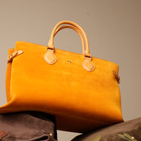 Yellow suede leather danilos handbag with brown handles and accents on a neutral background