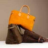 Two suede leather danilos  tote bag, one yellow and one brown, on a white surface with a beige background.