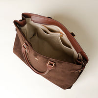 upper view of a opened Brown suede danilos leather tote bag with gold hardware on a light beige background