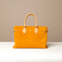 Yellow suede leather danilos  tote bag with tan handles and accents on a beige background