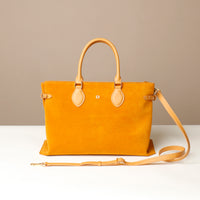 Yellow suede leather tote bag with a strap  and danilos  logo on a white surface against a beige background