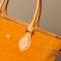 Close-up of a mustard yellow suede leather danilos  tote bag with leather accents on a neutral background