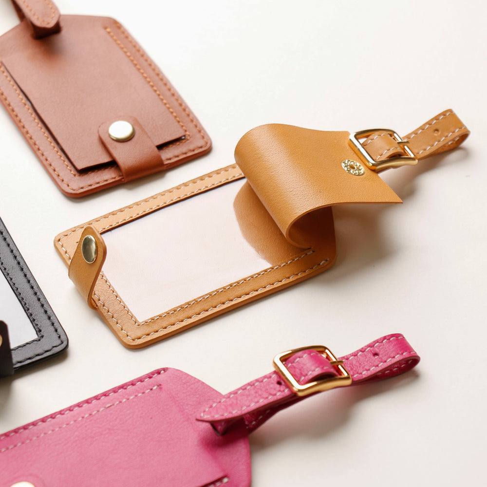 A collection of colorful leather travel tags in beige, brown, pink, and purple, displayed on a white surface.