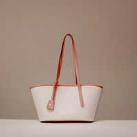 A structured tote bag with a light beige canvas body and warm brown leather trim and shoulder straps, displayed on a neutral beige background.