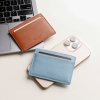 Brown and blue leather card holders on a white surface with a laptop and phone.