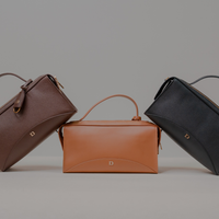 Three Avela Bag with top handle and detachable strap in brown, tan, and black on a gray background
