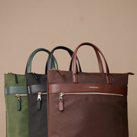Three TransitTrek crossbody, messenger bags in green, black, and brown on a beige background
