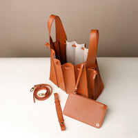 Brown leather handbag with matching strap and pouch on a white surface.